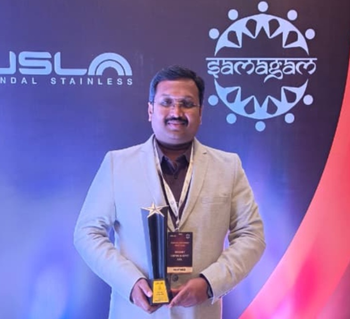 Man holding an award trophy at a Jindal Stainless corporate event stage with Samagam backdrop